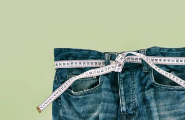 Yeşil arka planda mezurası olan kot pantolonlar. Kilo verme konsepti