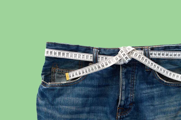 Jeans with a measuring tape on a green background. Weight loss concept