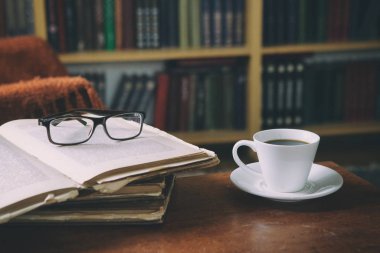 Kitaplar ve bir fincan kahveyle rahatlama anları. Koltukta kedisi olan bir adam. Eski kitaplar, gözlükler, kütüphane..