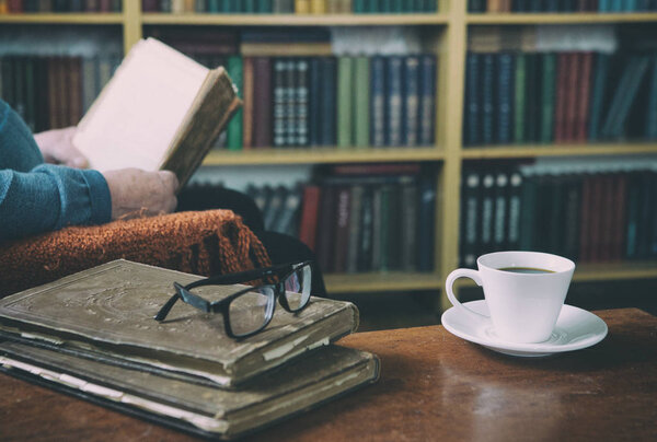 Sweet moments of relaxation with books and a cup of coffee. A man in an armchair with a cat. Vintage books, glasses, library.