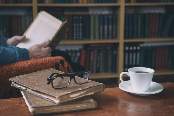 Sweet moments of relaxation with books and a cup of coffee. A man in an armchair with a cat. Vintage books, glasses, library.