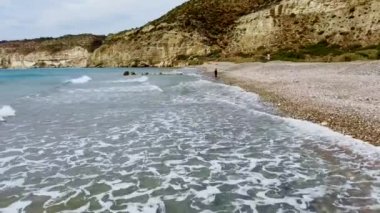 Çakıl taşlı bir plajda çıplak ayakla yürüyen genç bir kızın hava aracı görüntüsü.