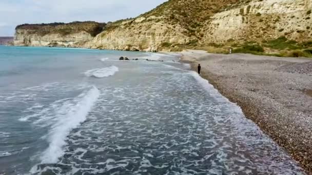 Aerial drone view of a young girl walking barefoot on a pebble beach — Stock Video