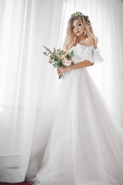 Les honoraires de la mariée à l'hôtel. Une belle blonde se tient à la fenêtre dans une robe de mariée . — Photo