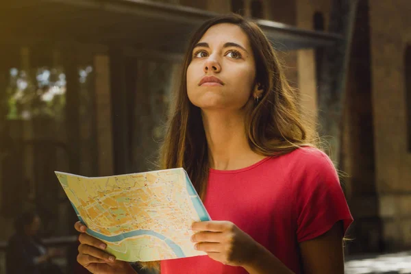 Tourist woman searching in a city map looking for a place in a urban background. Young traveler erasmus student girl lost