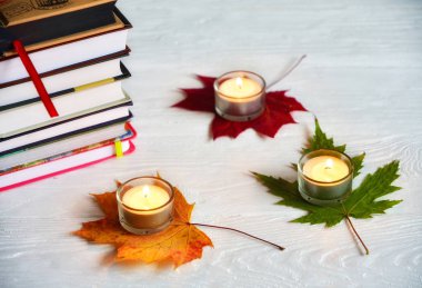 Kitaplar, mumlar ve kuru yapraklarla sonbahar arkaplanı.