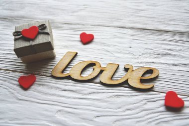 Küçük kırmızı kalpli hediye kutusu ve beyaz bir masada süslü tahta kelimelerle aşk. Sevgililer Günü arkaplanı.