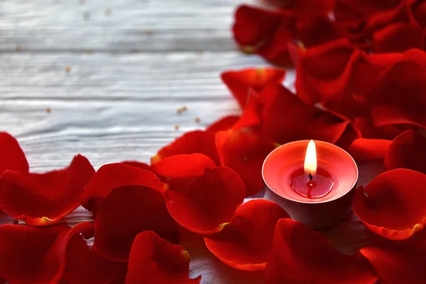 白い木の背景に赤いバラの花びらと赤い燃えるろうそく バレンタインデーの背景 — ストック写真