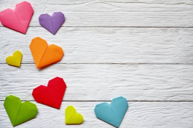 Beyaz ahşap arka planda çok renkli origami kağıt kalpler. Sevgililer Günü arkaplanı.