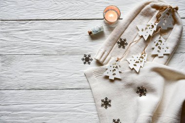 Beyaz ahşap arka planda Noel süsleri. Beyaz yün şapka ve eşarp, dantelli beyaz ahşap köknar ağaçları, gümüş kar taneleri, mum ve parıltılı dekoratif şişe. Kış arkaplanı.