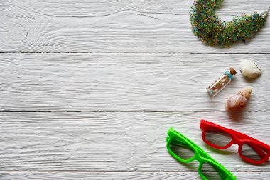 İki çift güneş gözlüğü, el yapımı boncuklar, deniz kabukları ve beyaz ahşap arka planda dekoratif şişe. Yaz arkaplanı.