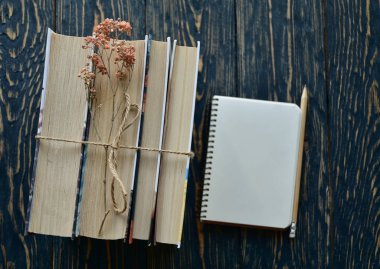 Bir yığın kitap, sicimle bağlanmış, kurumuş çiçekler ve siyah ahşap arka planda kalemle yazılmış bir defter. Üst Manzara. Yakın plan. Düz yatıyordu.