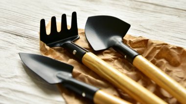 Evdeki bahçe işleri için aletler. İki küçük kürek ve tırmık el işi kağıdın ve beyaz ahşap arka planda yatıyor. Yan görüş. Yakın plan..