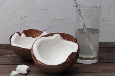 Tahta bir masada iki hindistan cevizi ve hindistan cevizi suyu dolu bir bardak.