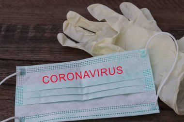 Tahta bir masada tıbbi koruyucu maske ve tek kullanımlık lastik eldivenler. Ağız ve burnu kaplayan tek kullanımlık cerrahi maske. Sağlık hizmetleri koronavirüsü karantina, hijyen konsepti