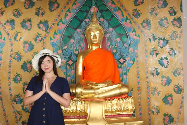 Asian beautiful girl wearing blue dress with white hat pray to the Buddha at Wat Arun in Bangkok, Thailand. Wat Arun is a famous tourist destination of Thailand. Travel concept