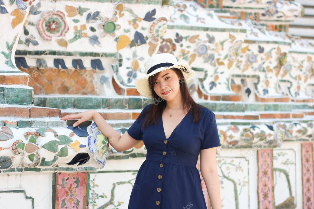 Asian beautiful girl wearing blue dress with white hat travel to Wat Arun in Bangkok, Thailand. Wat Arun is a famous tourist destination of Thailand. Travel concept