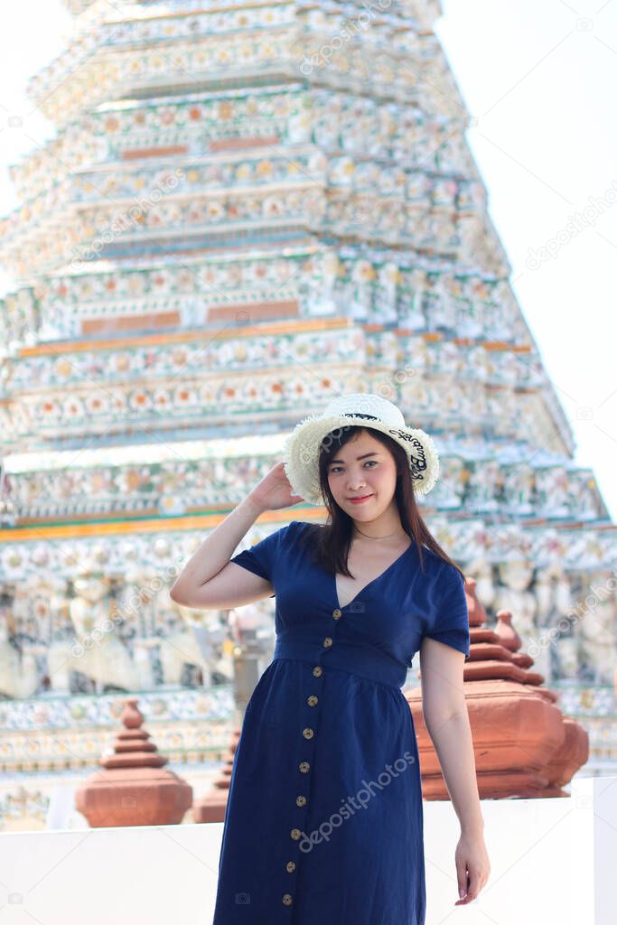 Asian beautiful girl wearing blue dress with white hat travel to Wat Arun in Bangkok, Thailand. Wat Arun is a famous tourist destination of Thailand. Travel concept