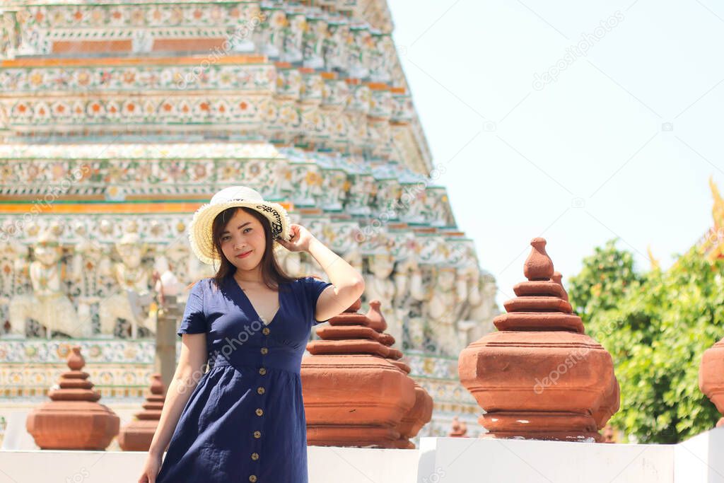 Asian beautiful girl wearing blue dress with white hat travel to Wat Arun in Bangkok, Thailand. Wat Arun is a famous tourist destination of Thailand. Travel concept