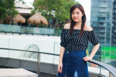 Genç kadın, Bangkok, Tayland 'da çatı katındaki mağazada poz veren ve gülümseyen siyah bir etek giyiyor. Kadınlar tatile çıktıklarında mutlu olurlar..