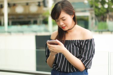 Asyalı güzel kız, erkek arkadaşıyla sohbet etmek için akıllı telefonu kullanıyor. Hafta sonu cep telefonuyla rahatlayan Asyalı bir kızın portresi