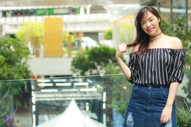 Asyalı güzel bir kızın portresi omuzlarındaki siyah bluzu ve binadaki bahçeli cam balkonun yanında duran kot eteği giyer. Asyalı kız model dışarıda..