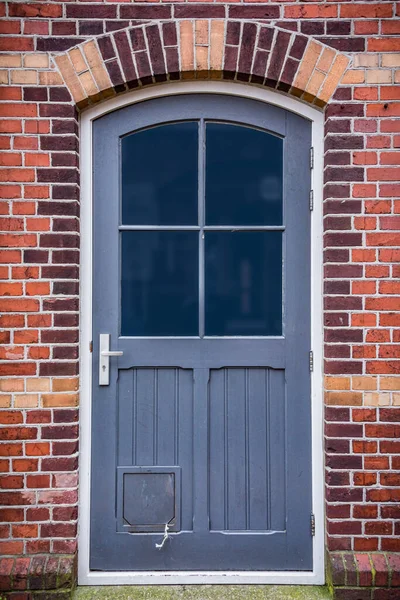 Szare drzwi z oknami w kamiennej ceglanej ścianie z klapką kota — Zdjęcie stockowe