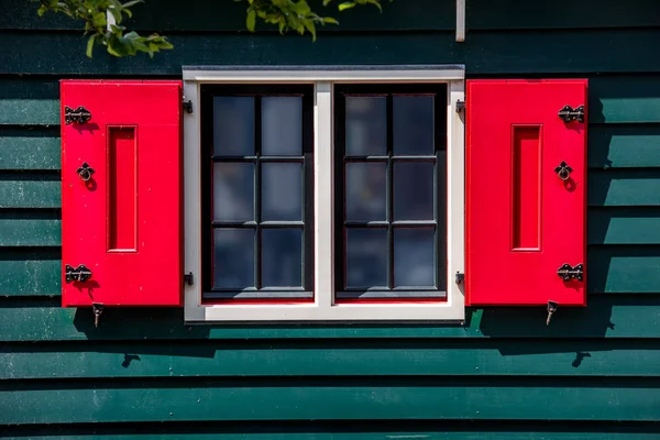 Élénk piros fa ablak redőnyök egy zöld fa fal — Stock Fotó