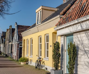 Amsterdam Holland, 20 Ocak 2020, Amsterdam North. Renkli evleri olan küçük bir cadde, sarı, kahverengi, gri, ön cephesi çiçekli ve güneşli bir sonbahar gününde binmek için bisikletli
