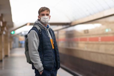 Genç adam, koruyucu bir tıbbi maske takmış metronun arka planında, tünelde tren bekliyor. Salgın konsepti, salgın virüsü