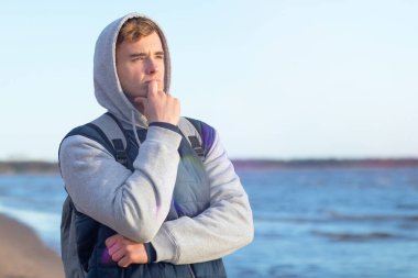 Close-up portrait, Pensive young man on the background of the bay. Handsome romantic guy is dreaming on the background of the sea clipart