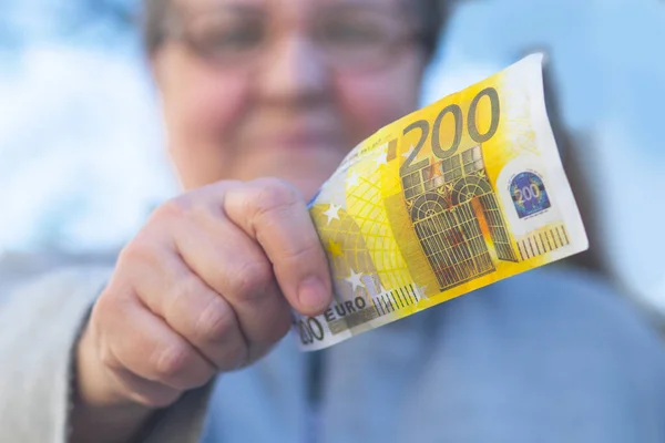 An elderly adult woman gives a currency of close-up 200 euros. Mature woman and holds out a bill. Senior female. Concept Retired pensioners and money.
