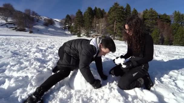 Děvče a chlapec dělají sněhuláka v horách. Šťastný pár vtipkování se sněhem