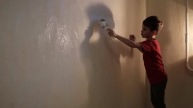 Çocuk beyaz boyayla bir duvarı fırçayla boyuyor. Video görüntüsü. Arkadan vurulmuş. 4K 'yı kapat.