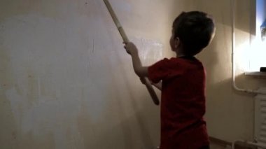 Çocuk uzun kabzalı bir silindirle duvarı beyaz boyayla boyuyor. Video görüntüsü. Arkadan vurulmuş. 4k