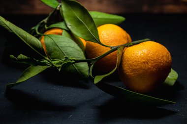 Karanlık bir yüzeyde yapraklı üç mandalina vardır..