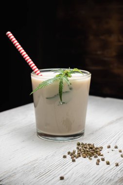 Kenevir tohumlarından alınan süt bir bardağa dökülür. Kenevir yaprağının yanında. Marihuana tohumlarının yanında. Koyu tahta arkaplan