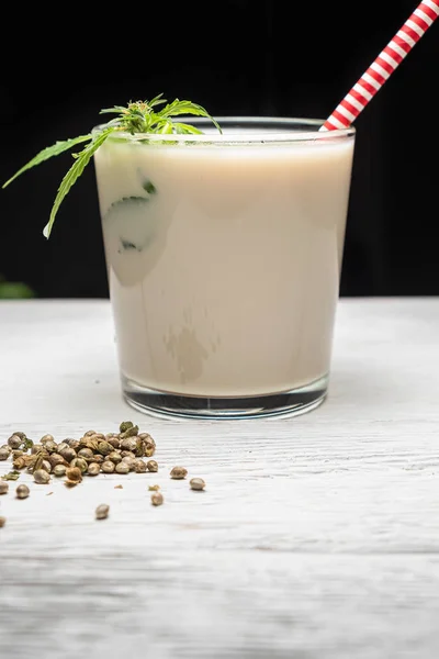 milk from hemp seeds is poured into a glass. Nearby cannabis leaf. Nearby marijuana seeds. Dark background