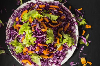 Kırmızı lahana salatası düz bir tabağın etrafına gelişigüzel dağılmış. Siyah arka plan. en üstteki görünüm.