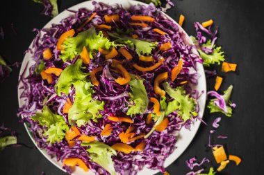 Kırmızı lahana salatası düz bir tabağın etrafına gelişigüzel dağılmış. Siyah arka plan. en üstteki görünüm.