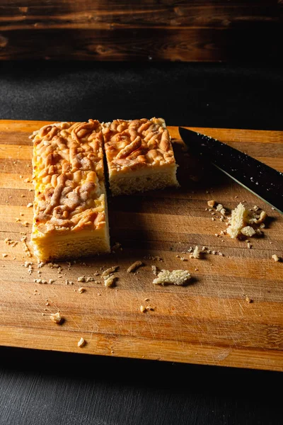 cut pie on a cutting board. three square pieces of four. lies on a striped old cutting board. A lot of crumbs. Near a large knife. On the black countertop.