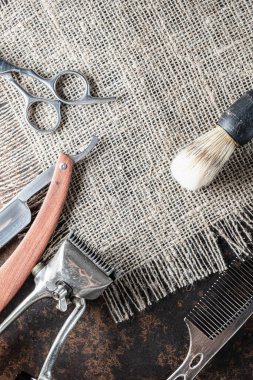 Klasik berber aletleri tehlikeli jilet, kuaför makası, eski manuel makas, metal tarak, tıraş fırçası. Kabataslak bir çuval üzerinde yalan söylüyor. Dikey. Üst görünüm, düz uzanma.
