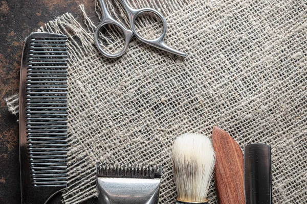 vintage barber tools dangerous razor, hairdressing scissors, old manual clipper, metal comb, shaving brush. Lies on a rough burlap sack background. Horizontal. top view, flat lay. copy space