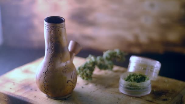 Bong fumant avec de la marijuana sur la table à côté est un broyeur et un grand bourgeon de cannabis médical. fond en bois . — Video