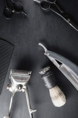 Siyah tozlu bir yüzeyde eski berber aletleri vardır. Klasik manuel saç kesme makinesi tıraş fırçası tıraş fırçası tıraş fırçası saç kesme makası. siyah monokrom. Dikey. Üst Manzara. düz yat.
