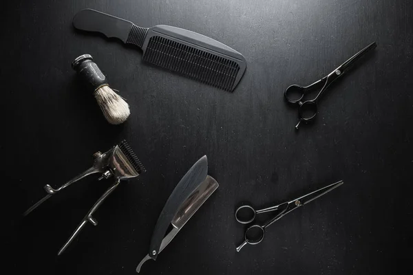 On a black dusty surface are old barber tools. Vintage manual hair clipper comb razor shaving brush shaving brush hairdressing scissors. black monochrome. horizontal. top view. flat lay.