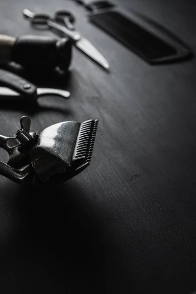 On a black dusty surface are old barber tools. Vintage manual hair clipper comb razor shaving brush shaving brush hairdressing scissors. black monochrome. vertical.