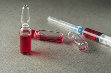 iki dolu ve bir boş ampul ve gri arka planda kırmızı ilaç olan bir şırınga. Yakın plan. Tıbbi iğnenin uzunluğu. Yatay yönelim