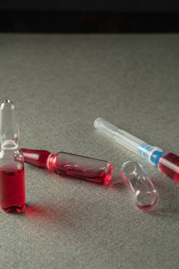 iki dolu ve bir boş ampul ve gri arka planda kırmızı ilaç olan bir şırınga. Yakın plan. Dikey yönelim