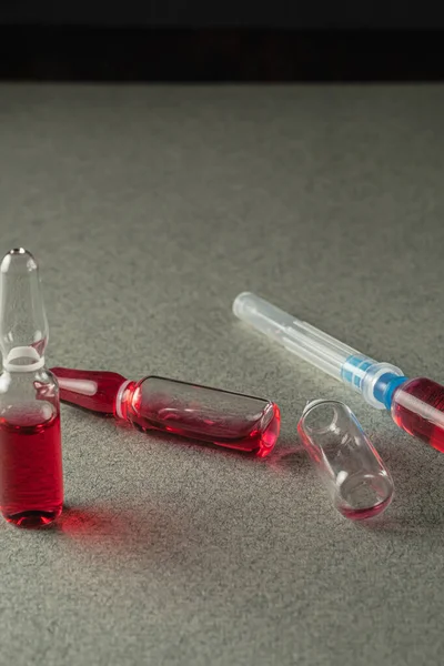 iki dolu ve bir boş ampul ve gri arka planda kırmızı ilaç olan bir şırınga. Yakın plan. Dikey yönelim